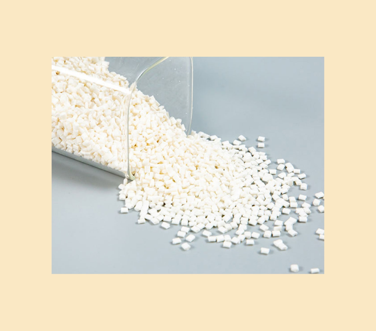 small white compostable modified resin pellets spilling from a clear container onto a gray surface.